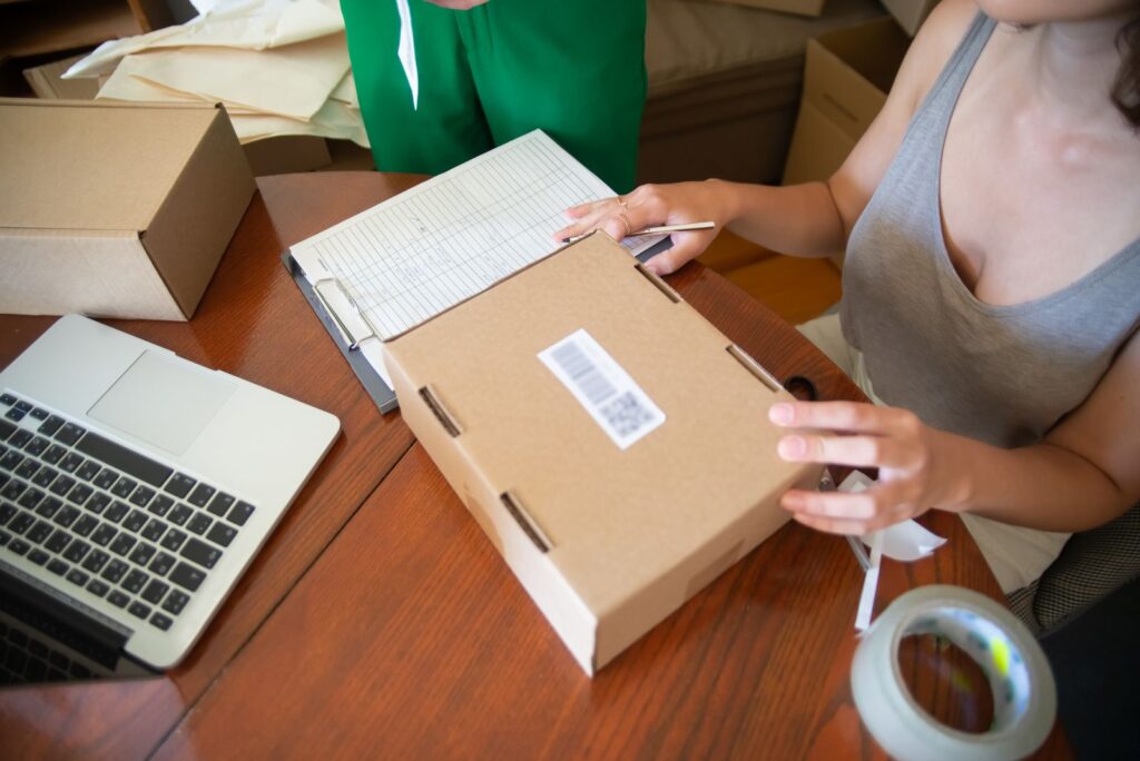 Two people packing online shop orders at a table with a laptop, a small ecommerce business at work