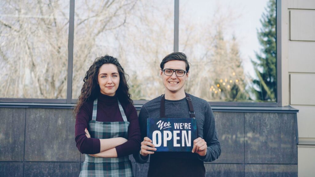 Two local business owners outside their shop holding an open sign, the kind of business local SEO helps customers find