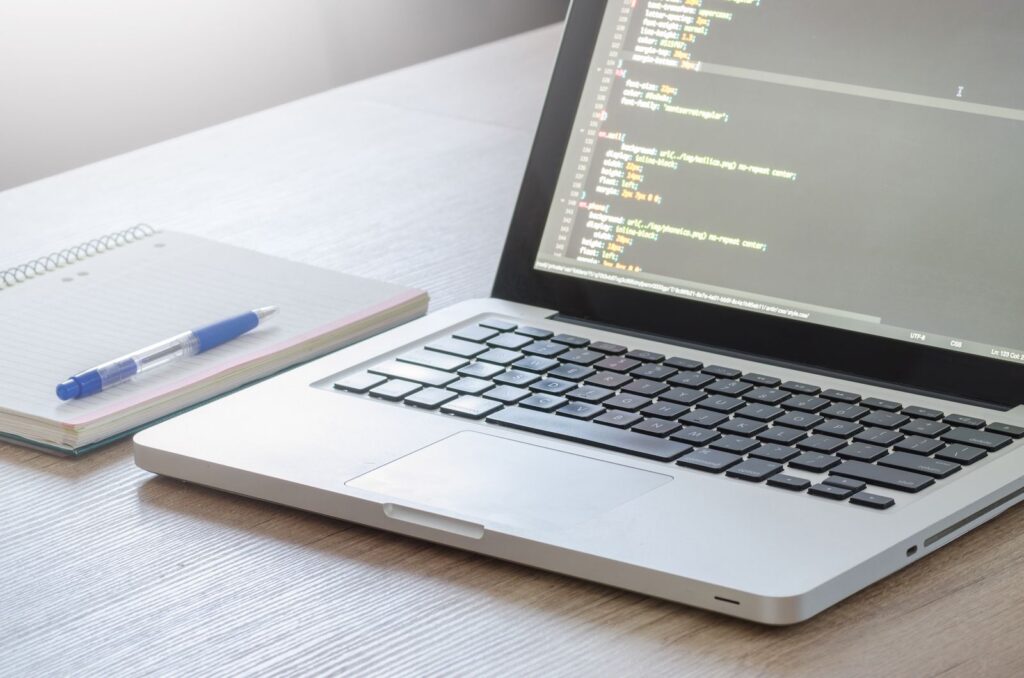 Laptop showing a code editor beside a notebook, building a WordPress website
